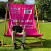 A person sitting in a custom-branded pink Giant Deckchair at an outdoor event, demonstrating the massive scale and comfort of the furniture