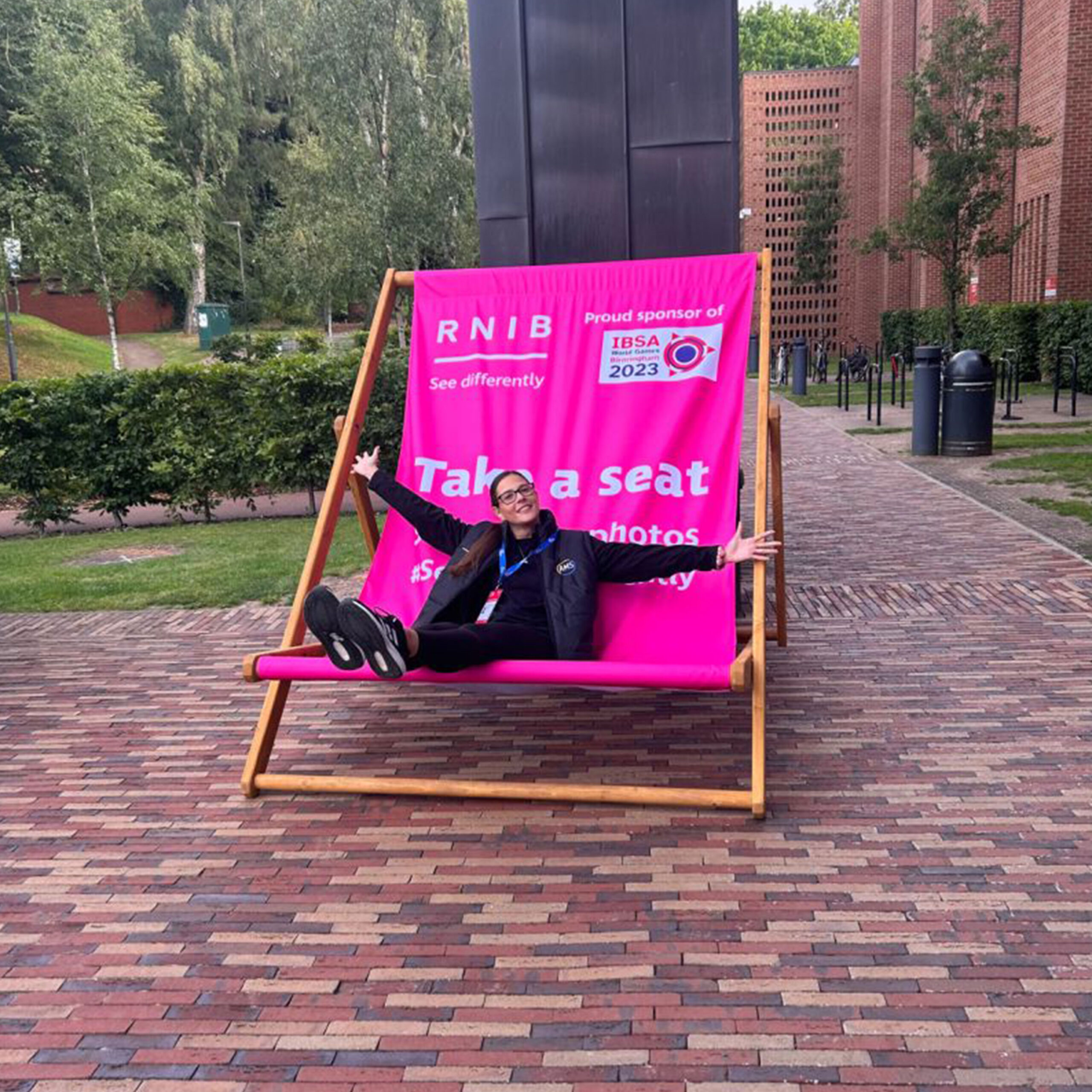 A person sitting in a custom-branded pink Giant Deckchair at an outdoor event, demonstrating the massive scale and comfort of the furniture