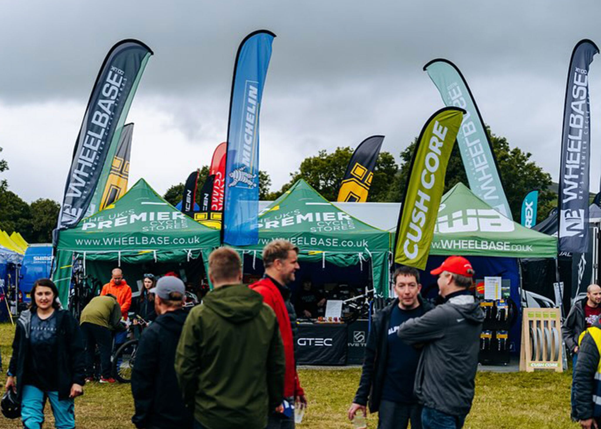An array of branded flags connected to multiple branded gazebos supplied from Surf & Turf Instant Shelters for Wheelbase at an outdoor bike event.